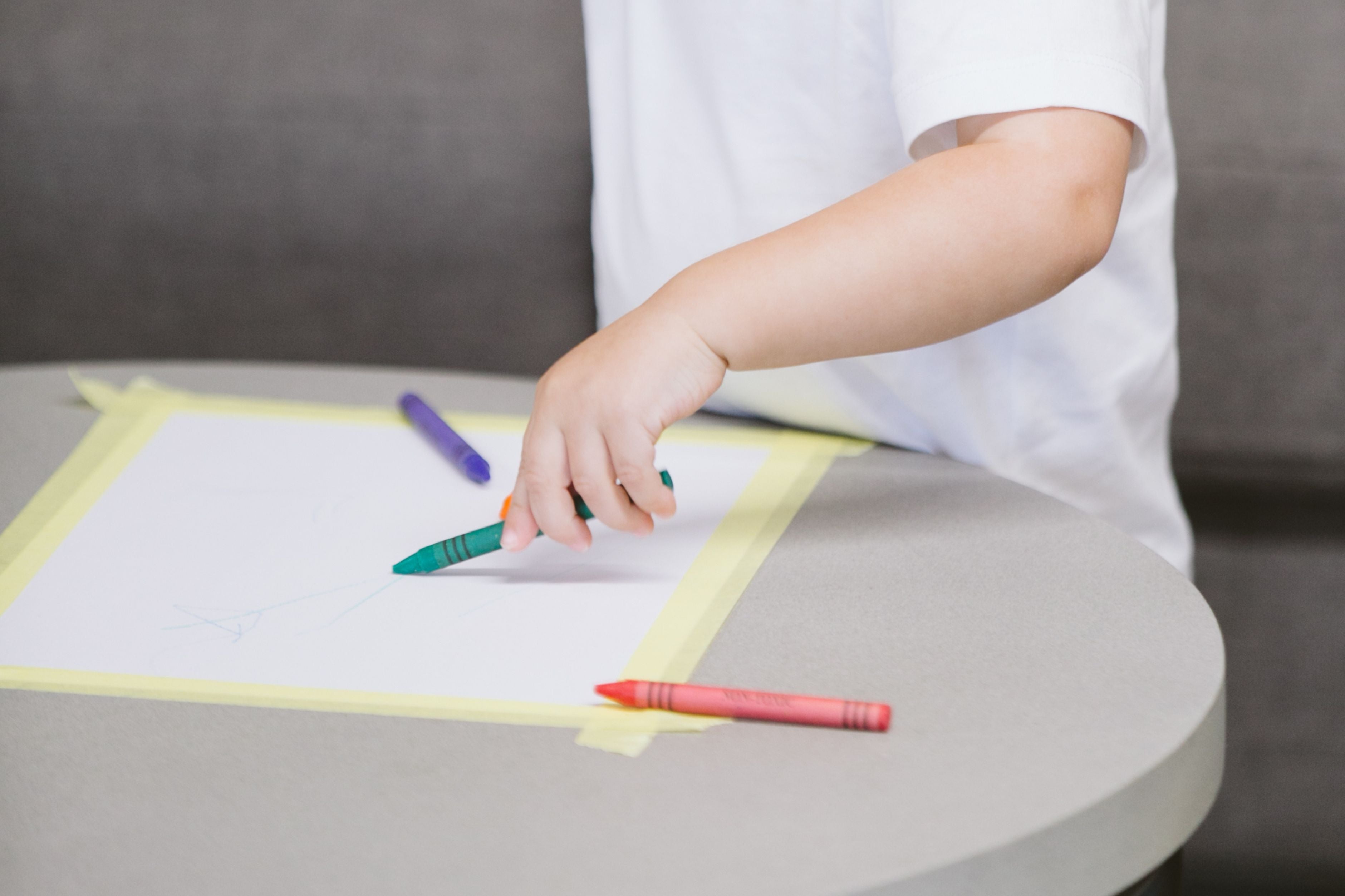 toddler reaching out for crayons to practice drawing skill on taped down paper