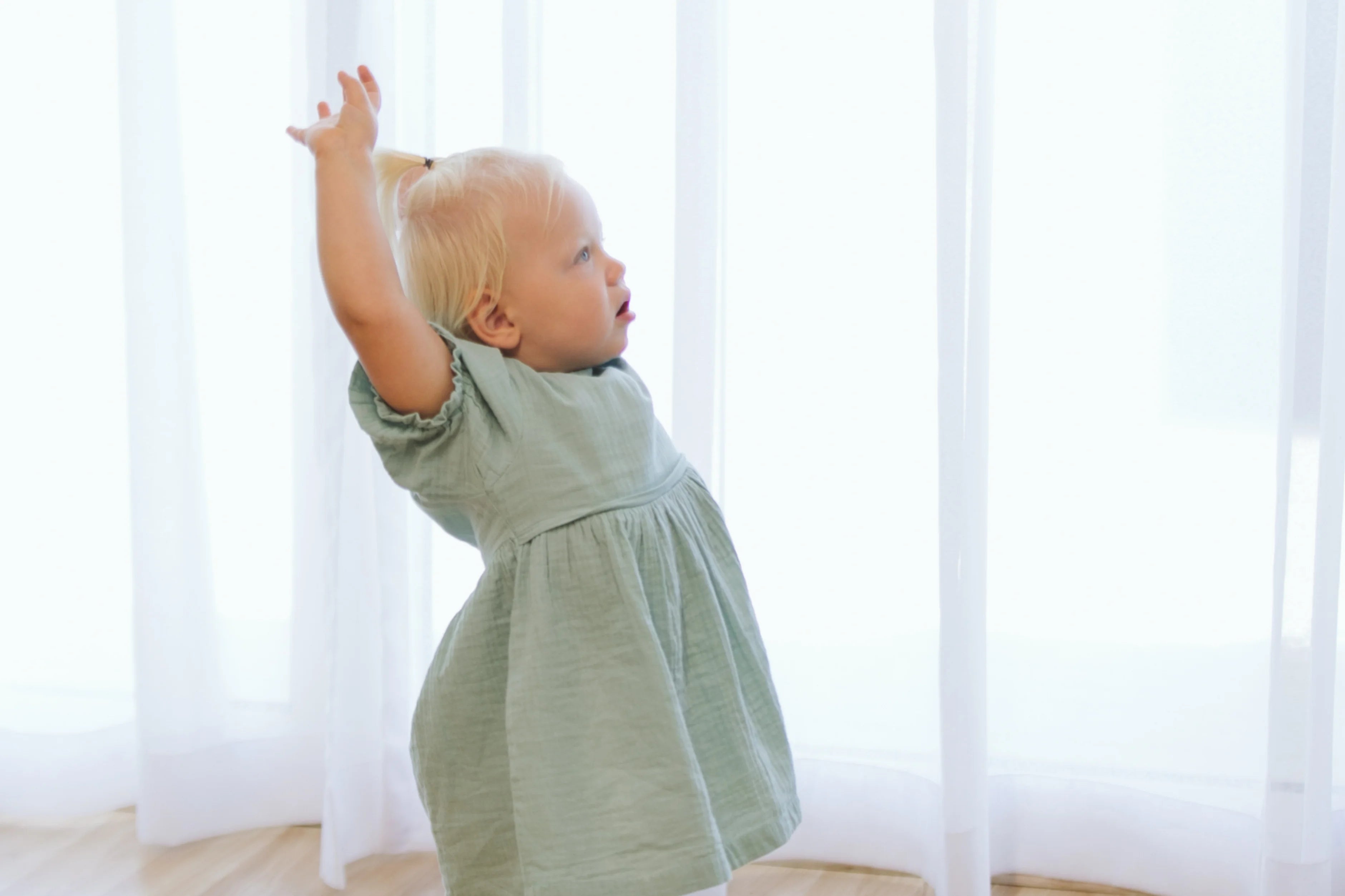 A toddler holding a soft ball above her head, illustrating engagement in physical play and motor skill development.