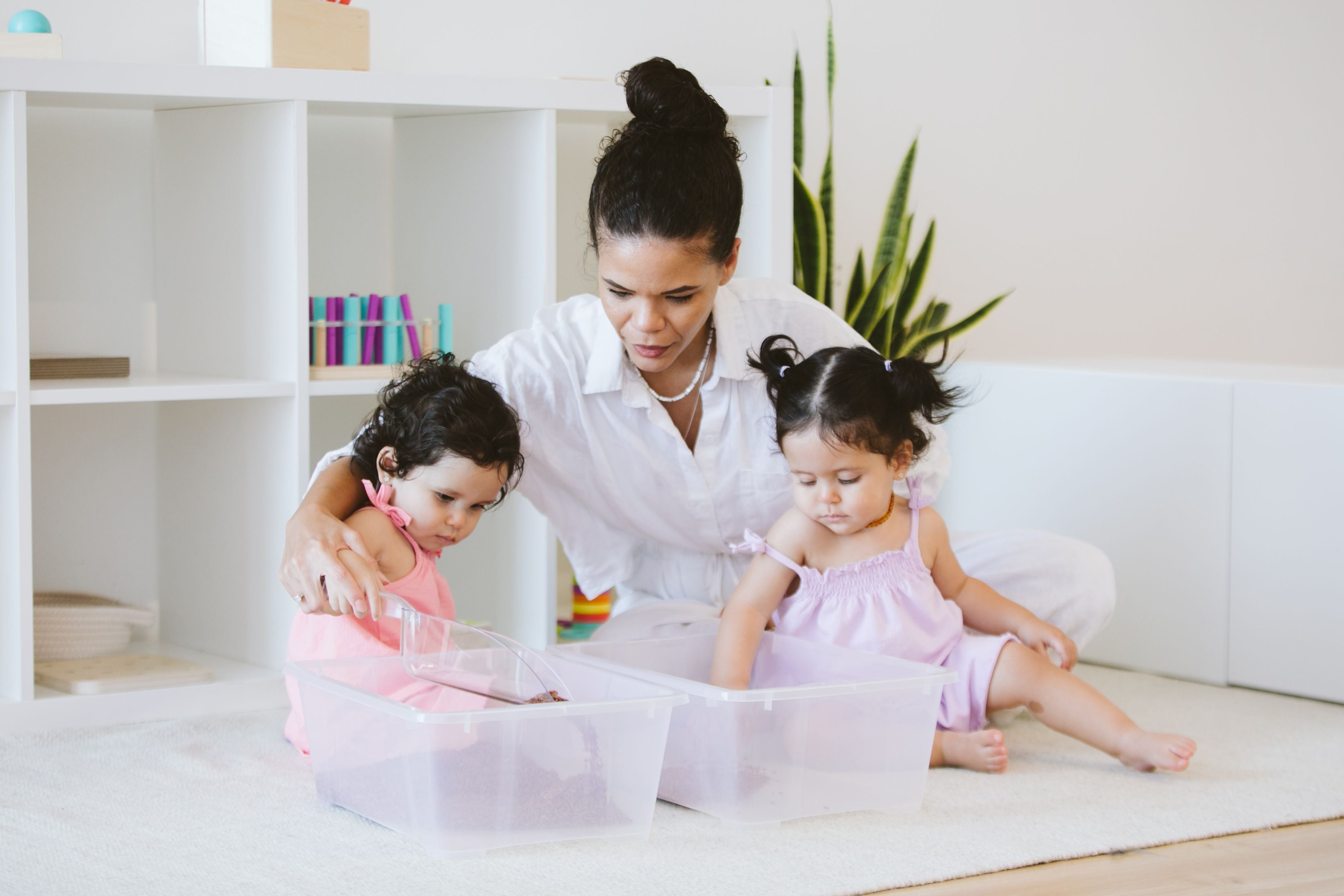 Parent and two toddlers arranging toys into different boxes, engaging in a sorting activity that promotes cognitive development and organizational skills.