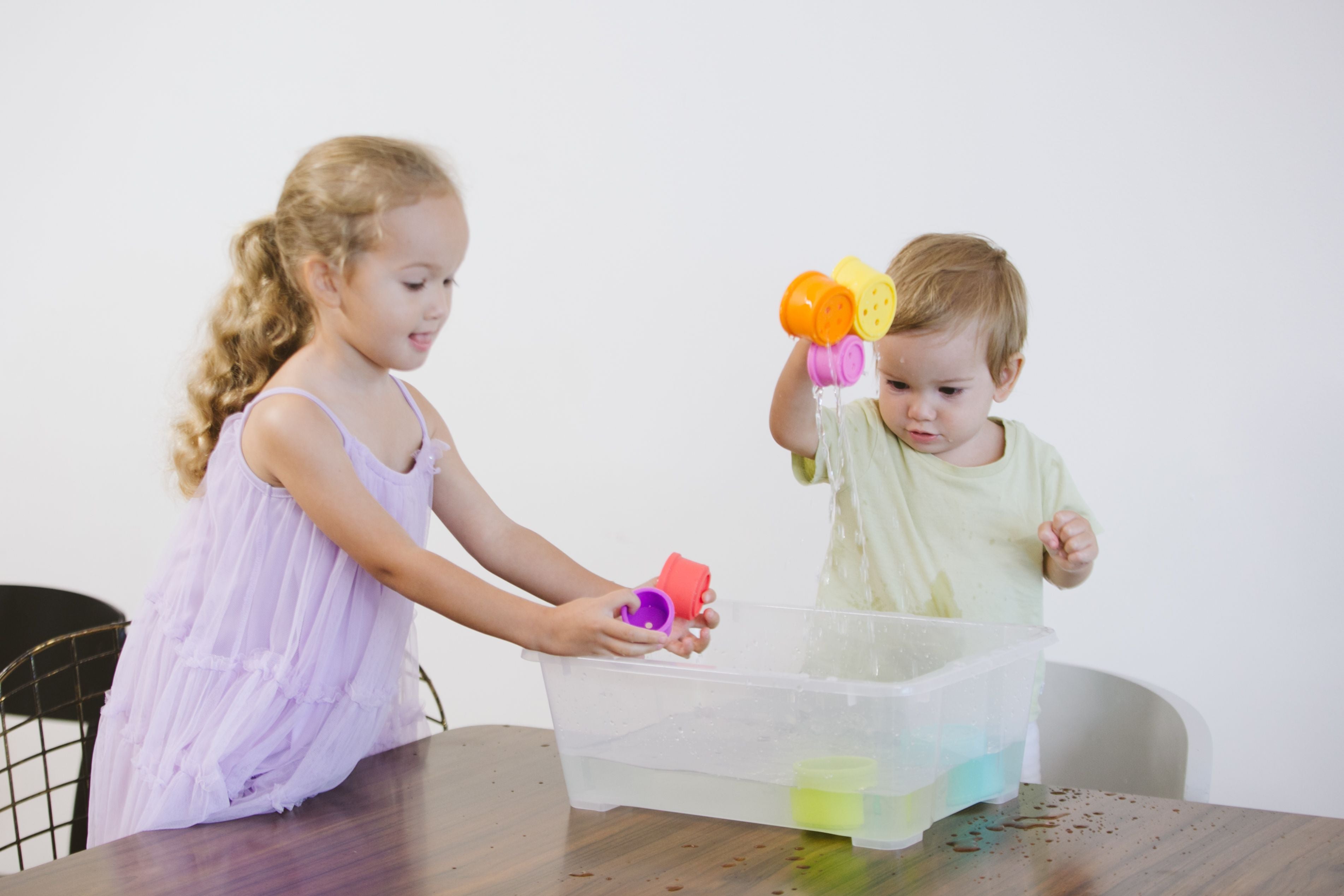 Two toddlers exploring and playing with toys taken out of a water sensory box.