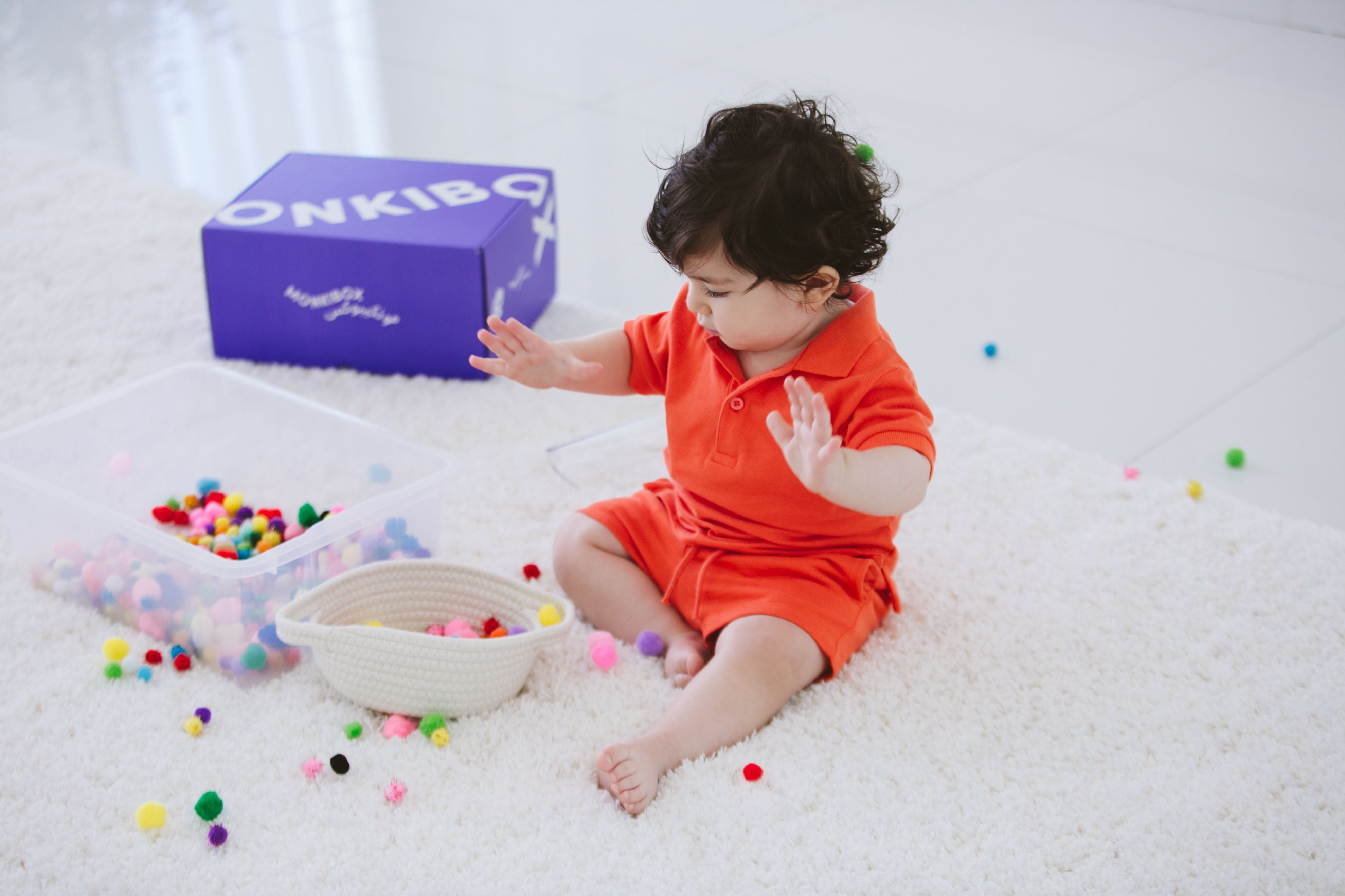 toddler plating with pompoms in treasure basket with a gift box