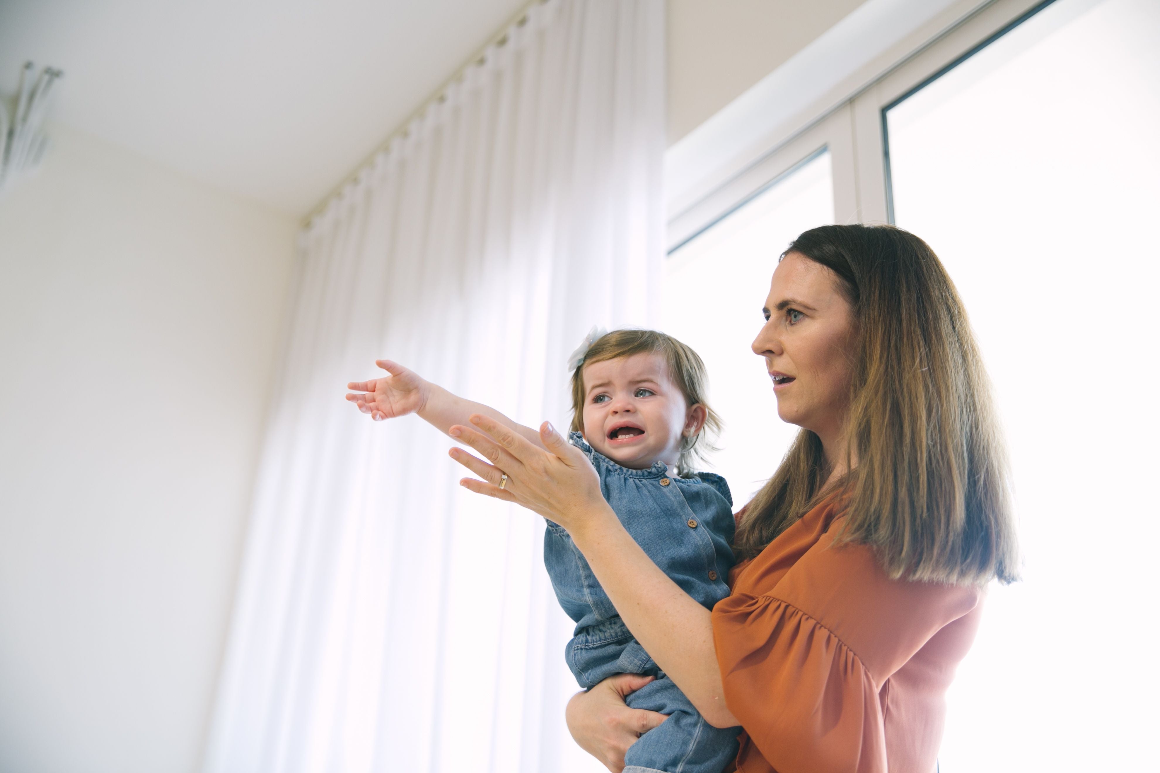 Mother holding a toddler while the child reaches out, illustrating frustration and emotional development during toddlerhood.